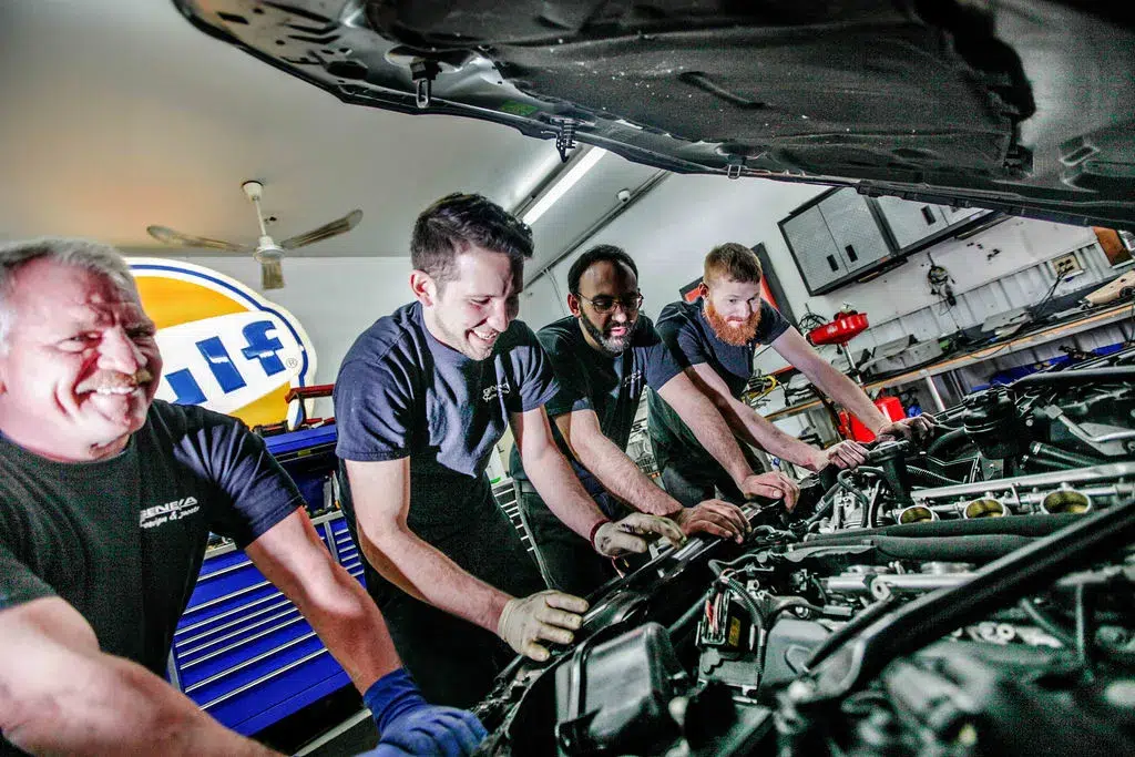 Mechanics leaning on an open vehicle smiling looking at an engine